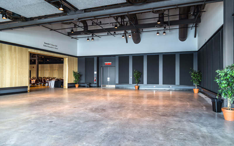 A wide-open space with tall ceilings and polished concrete flooring. On the left is an entrance to a banquet hall, and on the front and right side are two walls installed with sound absorbent panels.