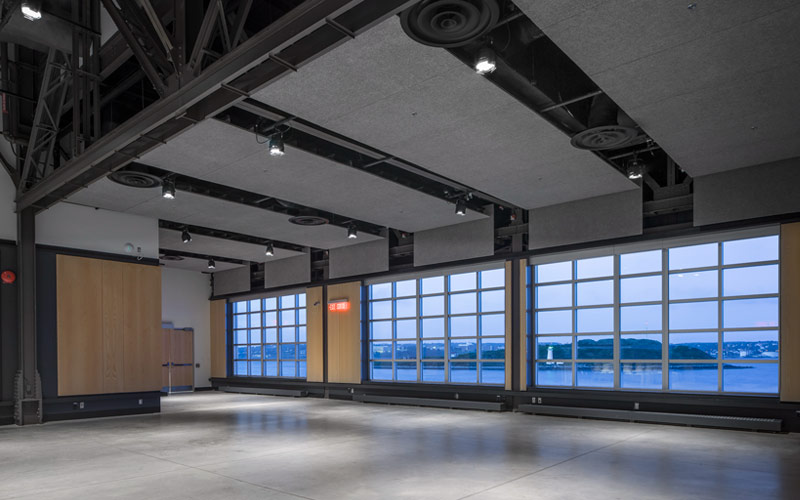 Floor to ceiling windows offer a view of the harbour and an island. The room has polished concrete flooring, and the ceiling is exposed.