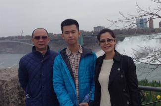 A young man stands between his parents with Niagara Falls in the background.